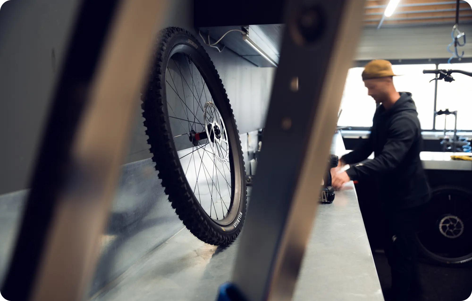 Mécanicien en train de travailler dans l'atelier Gravitylab, photographié en flou artistique derrière une roue de VTT au premier plan équipée d'un pneu Maxxis à crampons