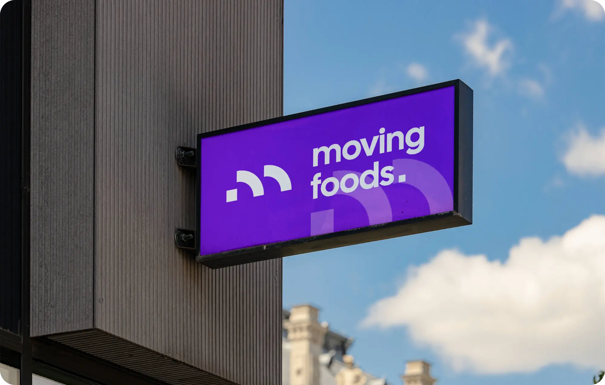 Enseigne lumineuse violette fixée en façade affichant le logo et le nom Moving Foods, photographiée en extérieur avec ciel bleu